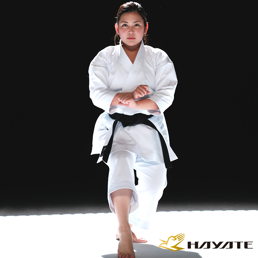 Person in a Hayate white martial arts uniform with a black belt on a black and white background, featuring the Hayate brand.