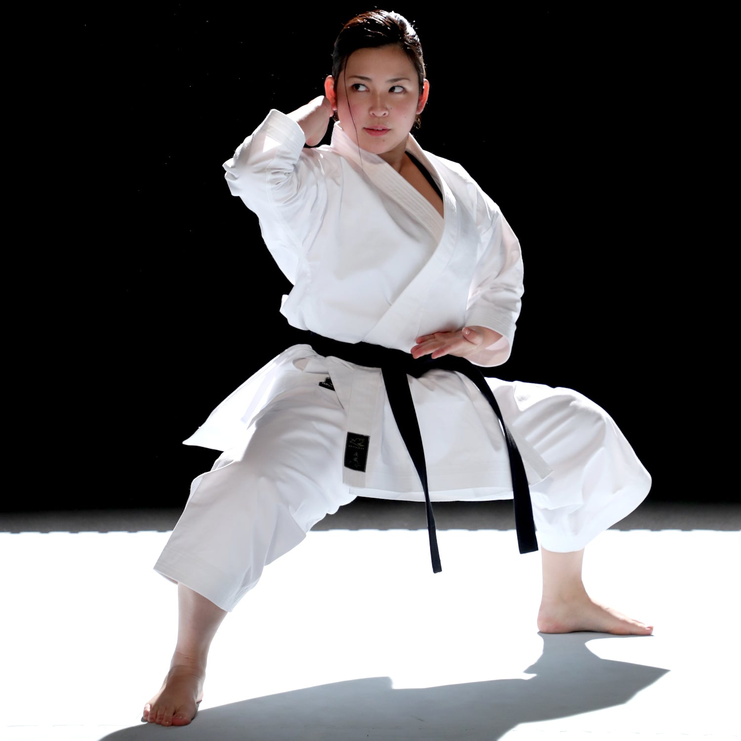 Person in a Hayate white martial arts uniform with a black belt performing a pose on a black and white background