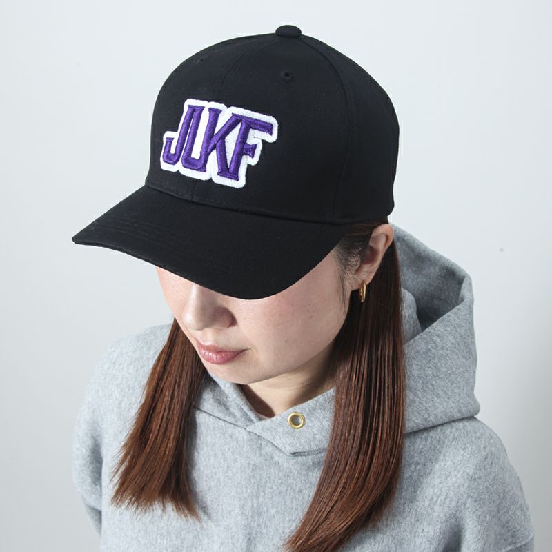 Person wearing a black cap with 'JUKF' in purple and white on a light gray background
