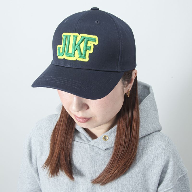 Person wearing a navy blue cap with 'JUKF' in yellow and green on a plain background